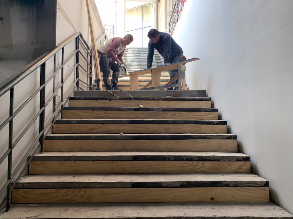 Equipo instalando revestimientos en una escalera interior durante la obra.